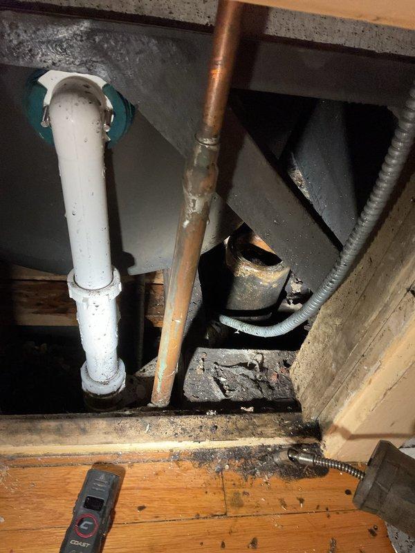 Responded to a bathtub drain clog on the middle floor of a century-old residence where the blockage had persisted for approximately five days. Accessed the drain system through the under-sink area, inspecting the existing plumbing infrastructure which consisted of white PVC drain lines with teal couplings and copper supply lines showing age-appropriate patina and minor corrosion at joints. Assessed the drain assembly and determined the clog location within the drainage system. Successfully cleared the obstruction using appropriate drain cleaning methods, restoring proper water flow to the bathtub. Verified all connections remained secure and tested the drain for proper function before completing the service call.