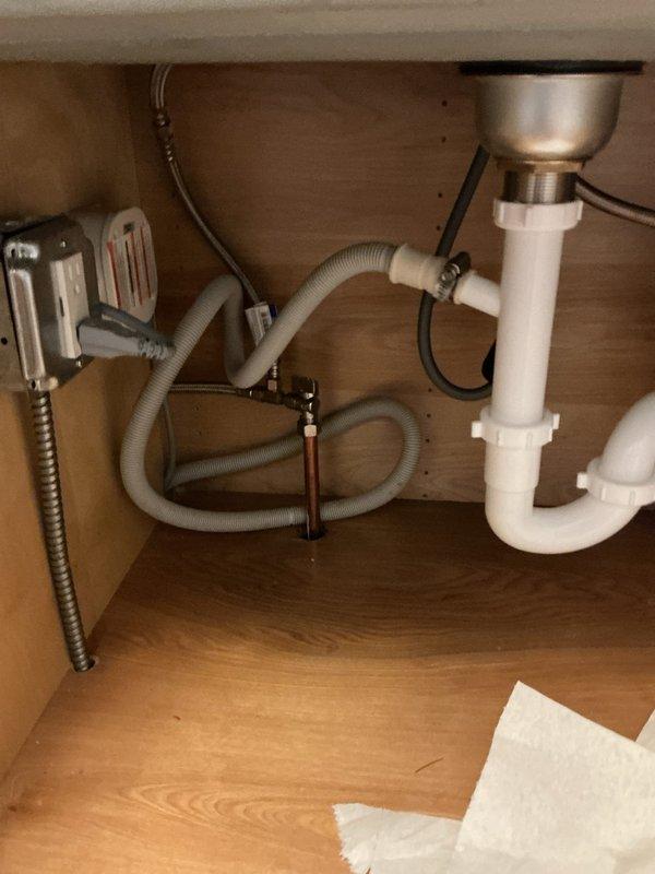 Responded to service call for kitchen faucet leak and under-sink leak in powder room. Inspected kitchen sink cabinet plumbing system, identifying moisture issues in P-trap assembly and supply line connections. Placed absorbent materials beneath plumbing fixtures to monitor leak sources and protect cabinet interior. Documented existing plumbing configuration including white PVC P-trap, metallic drain basket, chrome flexible supply lines, and associated dishwasher/disposal connections for further diagnostic assessment and repair recommendations.