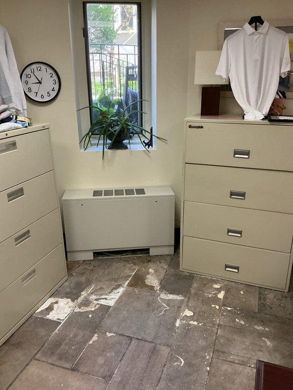 Responded to priority water leak located underneath stone tile flooring in office area. Upon arrival, conducted thorough visual inspection revealing extensive water damage and mineral deposits across gray tile flooring, with white residue patterns indicating active moisture intrusion beneath the surface. Documented damage conditions with photographic evidence showing affected areas concentrated around HVAC unit and floor corners. Protected work area with floor covering to prevent further contamination during assessment.