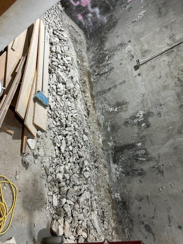 Completed plumbing repair requiring extensive demolition work to access compromised piping systems. Removed deteriorated concrete and plaster from basement wall to expose vertical conduits showing signs of water damage and corrosion. Debris removal and site preparation performed for upcoming pipe replacement and wall restoration work.