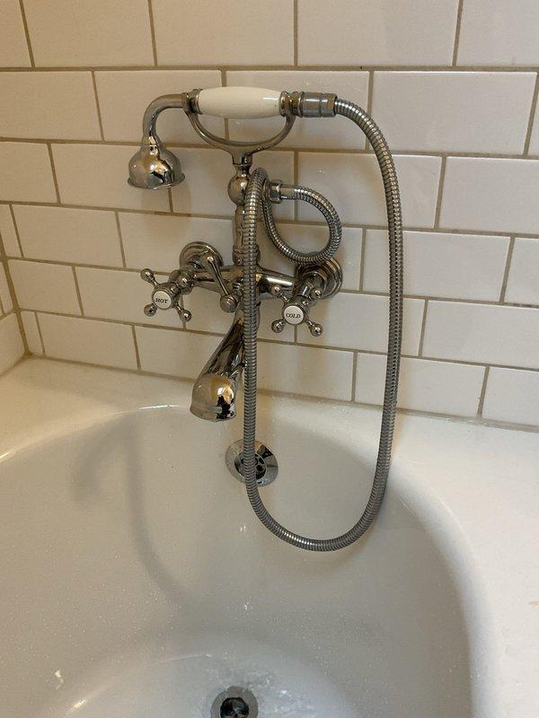 Responded to service call for water leaking from bathtub spout when toilet is flushed. Inspected bathroom plumbing fixtures including vintage-style tub faucet with cross-handle controls and handheld shower attachment. Examined basement plumbing system with exposed piping and drain lines to identify cross-connection or venting issue causing water to discharge through tub spout during toilet flush cycle. Documented existing plumbing configuration and fixture conditions. Provided estimate for necessary repairs to resolve improper drainage and prevent continued water diversion through bathtub spout.