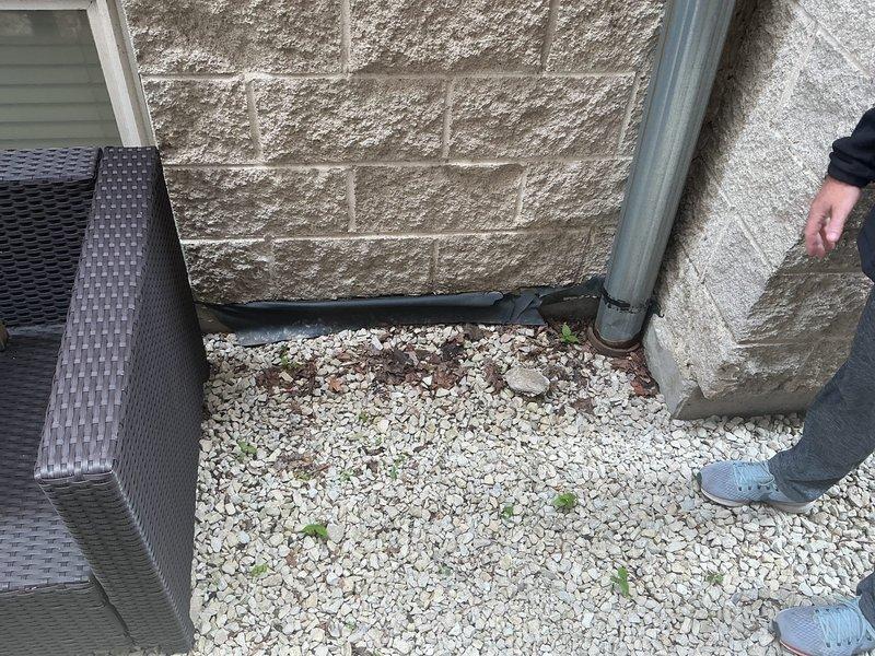 Conducted comprehensive site assessment for residential drain and sewer system issues. Evaluated downspout connection to main sewer line at building exterior, identifying potential drainage concerns where downspout discharge meets the underground system. Inspected mainline from rear to front of building to determine rodding requirements and assess blockage potential. Documented existing conditions with photographs showing downspout configuration, gravel drainage area, and connection points at building foundation for estimate preparation.