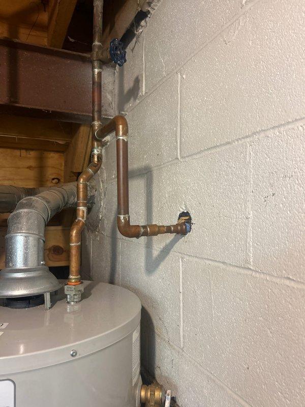 Responded to service call for leaking outdoor spigot and backed-up lavatory. Inspected exterior hose bib mounted on brick wall and identified active leak at connection point. Examined interior copper supply line routing from water heater area, including shut-off valve and associated fittings. Assessed plumbing configuration in utility room showing vertical and horizontal copper pipe runs with multiple elbow joints. Documented existing conditions of both interior supply infrastructure and exterior spigot installation for repair recommendations.