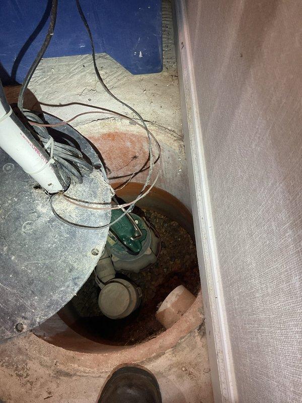 Performed comprehensive sump pump maintenance in residential basement utility area. Inspected sump pump pit, verified proper operation of green and white pump unit, and examined all electrical connections and wiring leading to the pit. Checked PVC discharge piping system, inspected pipe joints and connections including turquoise valve assembly at water heater area, and confirmed proper drainage flow. Evaluated gravel bed surrounding equipment, assessed concrete pit condition, and documented system components with photographic records to verify maintenance completion and equipment functionality.