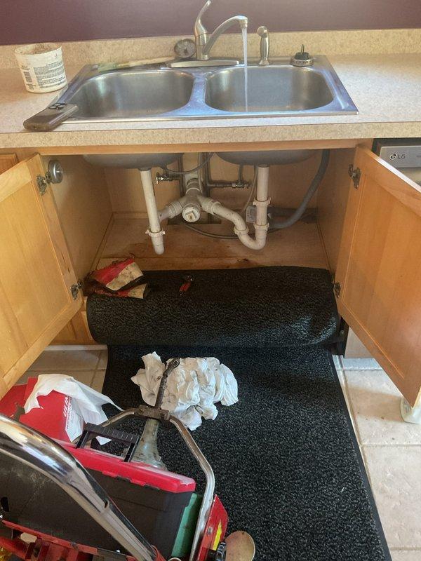 Responded to kitchen sink drainage issue affecting lower unit when upper unit fixtures were in use. Upon inspection, identified improper venting in the shared drain line causing backflow conditions between units. Accessed cabinet plumbing assembly and cleared obstruction from P-trap and connecting drain pipes. Removed accumulated debris and buildup from PVC drain system. Tested drainage flow from both upper and lower unit fixtures to verify proper operation and confirm elimination of backup condition. System functioning properly upon completion with no further backflow issues observed.