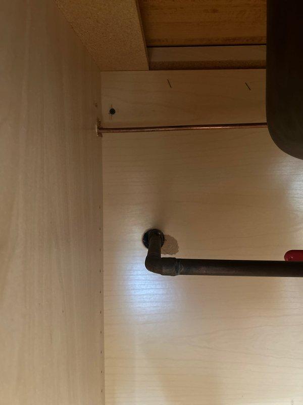 Responded to service call for dripping rooftop spigot. Upon investigation, traced the water supply line from the outdoor spigot through interior plumbing system. Inspected shutoff valve assembly with red-handled ball valve connected to copper supply lines showing oxidation. Accessed cabinet space beneath fixture to examine pipe connections, including black iron pipe elbow fitting and copper supply line with mounting bracket. Replaced worn washer and stem assembly in outdoor spigot to eliminate dripping condition. Tested shutoff valve operation and verified all connections for proper seal. System restored to full functionality with no active leaks detected.