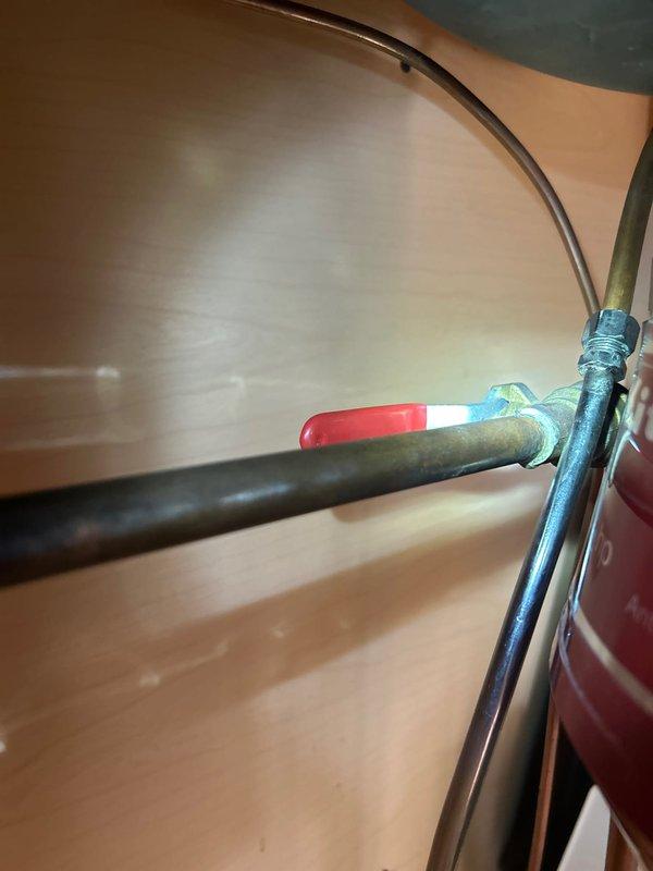 Responded to service call for dripping rooftop spigot. Upon investigation, traced the water supply line from the outdoor spigot through interior plumbing system. Inspected shutoff valve assembly with red-handled ball valve connected to copper supply lines showing oxidation. Accessed cabinet space beneath fixture to examine pipe connections, including black iron pipe elbow fitting and copper supply line with mounting bracket. Replaced worn washer and stem assembly in outdoor spigot to eliminate dripping condition. Tested shutoff valve operation and verified all connections for proper seal. System restored to full functionality with no active leaks detected.