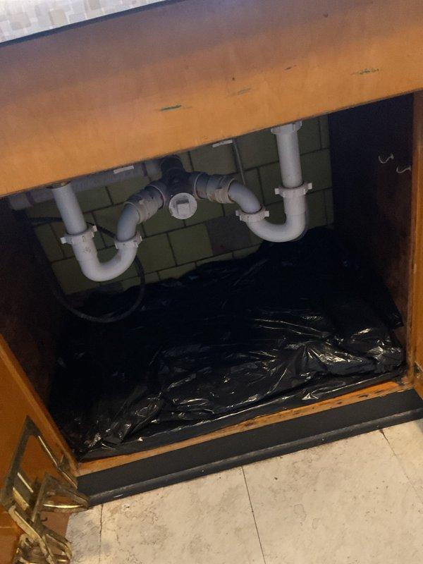 Responded to plumbing service call for drainage system inspection and maintenance. Accessed under-sink plumbing cabinet to examine P-trap configuration and drain connections, verifying proper installation and checking for leaks or blockages in the white PVC piping system. Located and inspected exterior sewer cleanout access port in lawn area, noting weathered condition of the bronze metal cleanout cap with oxidized patina. Verified cleanout accessibility for future maintenance needs and confirmed proper drainage system function throughout the property.