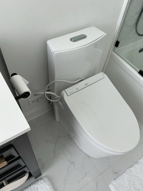 Responded to report of leaking toilet in unit 2107. Upon inspection, identified water leak originating from behind toilet with electronic bidet seat attachment. Diagnosed failed wax ring seal and loose tank-to-bowl connection as source of ongoing leak. Shut off water supply, disconnected bidet power and water line, removed toilet from flange, and replaced deteriorated wax ring with new seal. Inspected flange for damage, confirmed structural integrity, and reinstalled toilet with new brass closet bolts. Reconnected bidet water supply line with new braided stainless steel connector, verified all connections were properly tightened and sealed. Restored water supply, tested flush mechanism and dual-flush system for proper operation, and monitored for leaks during multiple flush cycles. Confirmed bidet seat functionality and verified no water discharge at base or supply connections. Left work area clean and all fixtures operational.