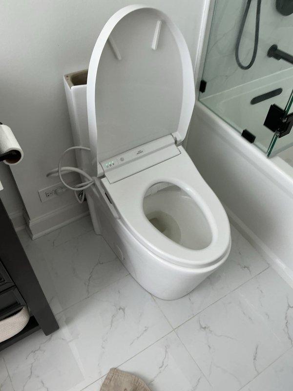 Responded to report of leaking toilet in unit 2107. Upon inspection, identified water leak originating from behind toilet with electronic bidet seat attachment. Diagnosed failed wax ring seal and loose tank-to-bowl connection as source of ongoing leak. Shut off water supply, disconnected bidet power and water line, removed toilet from flange, and replaced deteriorated wax ring with new seal. Inspected flange for damage, confirmed structural integrity, and reinstalled toilet with new brass closet bolts. Reconnected bidet water supply line with new braided stainless steel connector, verified all connections were properly tightened and sealed. Restored water supply, tested flush mechanism and dual-flush system for proper operation, and monitored for leaks during multiple flush cycles. Confirmed bidet seat functionality and verified no water discharge at base or supply connections. Left work area clean and all fixtures operational.