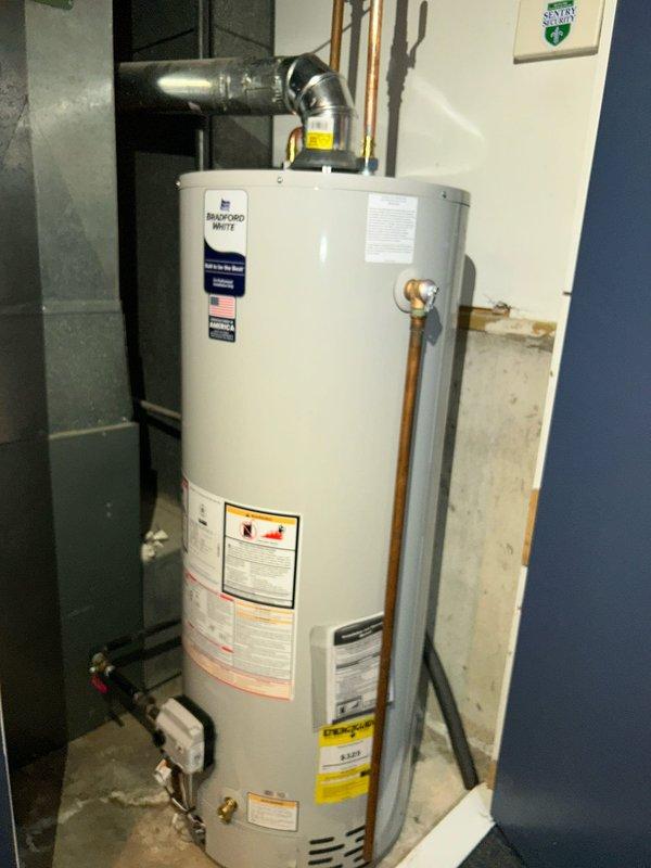 Completed installation of Bradford White tanked water heater in residential basement utility area. Unit was properly positioned and secured, with all required plumbing connections established including copper supply lines, brass fittings, pressure relief valve, and drain connections. Flexible metallic ductwork was installed and connected to facilitate proper ventilation and exhaust. All manufacturer specifications, safety labels, and energy guide information remain visible and intact on the unit for future reference and compliance purposes.
