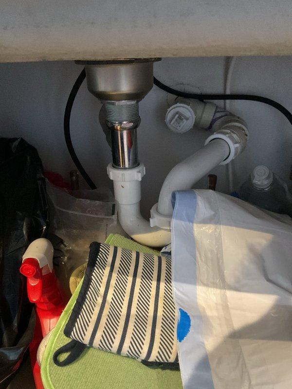 Responded to service call for kitchen sink backing up. Upon arrival, accessed plumbing beneath double-bowl sink and inspected drainage system including chrome drain assembly, white plastic P-trap, and connecting pipes. Cleared blockage from drain line, restoring proper water flow and drainage function. Verified all connections secure and tested system to ensure complete resolution of backup issue.