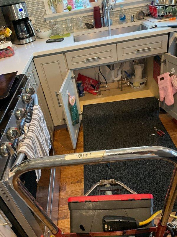 Responded to service call for kitchen sink backing up. Upon arrival, accessed plumbing beneath double-bowl sink and inspected drainage system including chrome drain assembly, white plastic P-trap, and connecting pipes. Cleared blockage from drain line, restoring proper water flow and drainage function. Verified all connections secure and tested system to ensure complete resolution of backup issue.