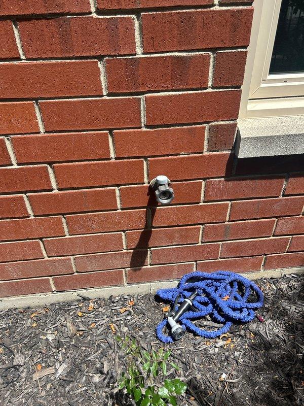 Responded to report of exterior sillcock leak causing interior first-floor carpet saturation. Upon inspection, identified failed or leaking outdoor hose bib mounted on brick exterior wall as source of water intrusion. Assessed interior damage to carpeted area near window, confirming moisture penetration through wall cavity from compromised sillcock. Documented exterior fixture condition and interior water damage with photographs for record.