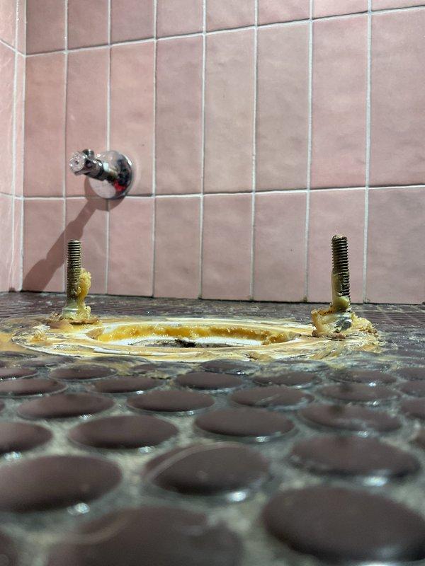 Responded to priority plumbing service call requiring two-person crew for bathroom floor drain repair. Upon arrival, assessed deteriorated drain assembly in tiled shower area showing significant mineral buildup, corrosion, and discoloration around the drain opening. Removed existing corroded drain cover with brass mounting bolts exhibiting greenish-yellow patina from prolonged water exposure. Cleaned drain opening and surrounding area of accumulated mineral deposits and staining. Installed new drain assembly with corrosion-resistant hardware to ensure proper water flow and prevent future deterioration. Verified proper drainage function and sealed installation. Work area left clean with all debris removed.