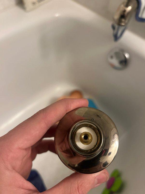 Serviced bathroom lavatory faucet with three-handle chrome fixture showing signs of age and tarnishing. Disassembled center dome cap to access valve stem assembly and inspect internal components for proper operation. Documented existing fixture condition including worn chrome finish and brass valve mechanism. Completed fixture maintenance and reassembly to restore functionality.
