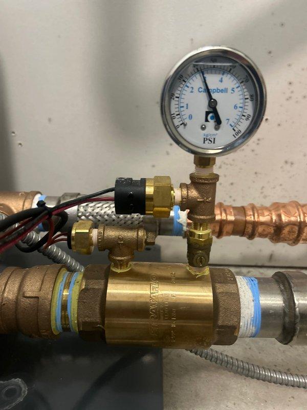 Performed diagnostic inspection of water pressure regulation system and hydronic plumbing assembly. Documented existing pressure gauge, brass fittings, copper piping with visible patina, check valve, and braided flex connections. Required replacement part has been identified and is currently available in shop inventory; follow-up appointment needed to complete installation and restore system to proper operating condition.
