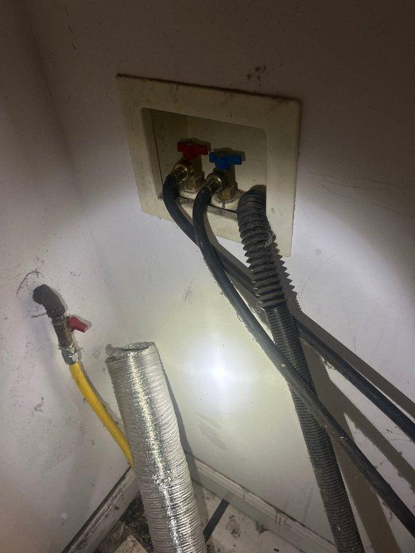 Responded to service call for leaking washing machine water supply valves. Upon inspection, identified compromised shut-off valves with red and blue handles mounted in recessed wall box showing active leakage at connection points. Provided detailed estimate for valve replacement and repair of associated supply line connections to resolve water leak issue and restore proper shutoff functionality.