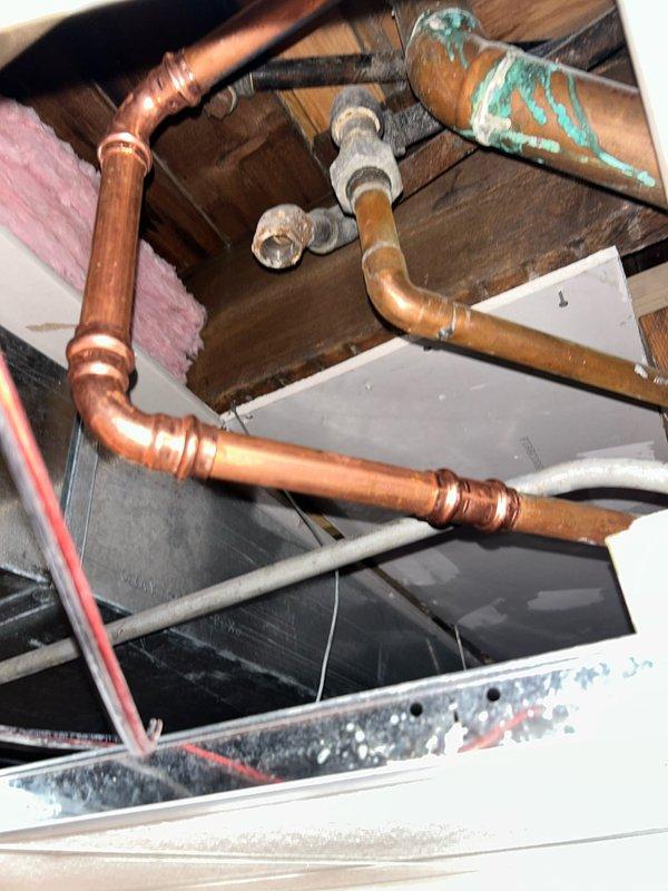 # Plumbing Service - Water Leak

Responded to active water leak in 120-year-old three-flat residential building where water was penetrating from second floor into first floor, causing ongoing damage over a six-day period. Upon arrival, accessed ceiling cavity and attic space to locate source of leak. Inspected extensive copper plumbing system showing significant age-related deterioration, including green patina formation and corrosion on multiple pipe sections. 

Traced leak path through wooden joists and framing members in ceiling space, identifying compromised piping near HVAC components and gray metal ductwork. Examined multiple pipe joints, fittings, and connections throughout the affected area. Documented existing conditions including aged copper pipes with varying degrees of oxidation, exposed wooden structural members with water staining, and insulation materials in proximity to plumbing lines.

Investigated second-floor bathroom directly above affected area, inspecting toilet i