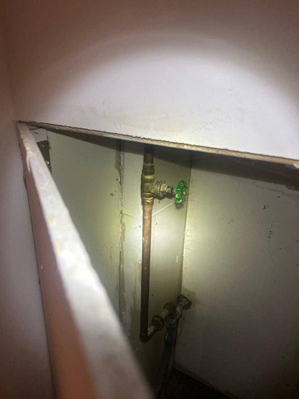 Installed plumbing fixtures including copper supply lines with brass shut-off valves featuring cross-handle controls. Mounted wall-based auxiliary lighting fixture with electrical connection to support work area visibility in mechanical access space.