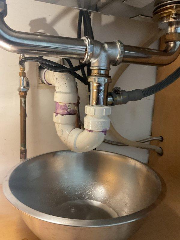 Responded to kitchen sink drainage issue in century-old home where homeowner had attempted P-trap cleaning but was unable to clear blockage completely or achieve proper reseal of the assembly. Upon inspection, found misaligned press-fit P-trap connections preventing proper seating and seal integrity. Disassembled white PVC P-trap assembly and chrome drain fittings, cleared remaining debris from trap and tailpiece, and realigned all connections to ensure proper fit and seal. Verified drainage flow, tested all connections for leaks, and confirmed P-trap reinstallation with appropriate water seal to prevent sewer gas entry.