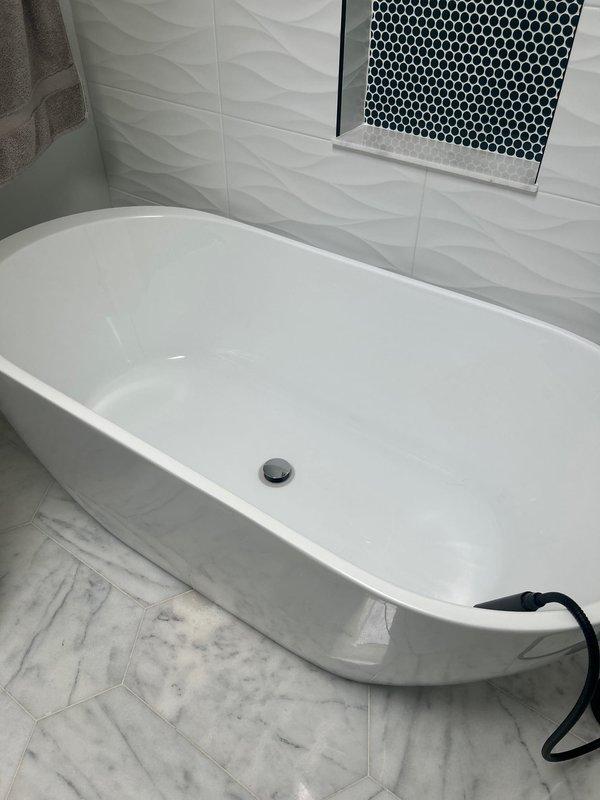 Completed installation and testing of modern freestanding bathtub in updated bathroom with marble-patterned hexagonal tile flooring and textured white ceramic wall tile. Verified proper water circulation, drainage functionality, and confirmed all fixtures operating correctly with no leaks detected.