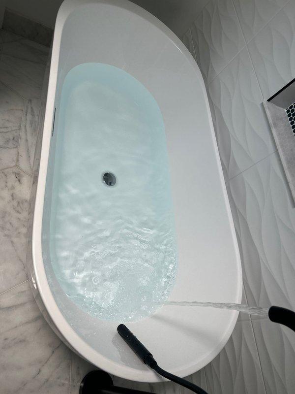 Completed installation and testing of modern freestanding bathtub in updated bathroom with marble-patterned hexagonal tile flooring and textured white ceramic wall tile. Verified proper water circulation, drainage functionality, and confirmed all fixtures operating correctly with no leaks detected.
