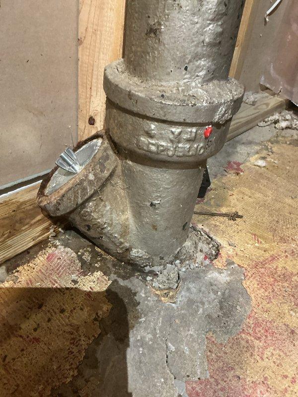 Responded to callback for plumbing system inspection in basement area with reported water infiltration issues. Upon arrival, documented severely deteriorated cast iron drain stack assembly showing extensive corrosion, pitting, and mineral deposits throughout all visible sections. The vertical and horizontal pipe connections exhibited heavy surface degradation with white calcium buildup indicating prolonged moisture exposure and age-related deterioration of the cast iron material.

Assessed active water damage on concrete basement floor with multiple wet areas and discoloration patterns. Placed absorbent materials at base of central plumbing stack to contain ongoing moisture. Photographed condition of corroded flanged connections and T-joints for documentation purposes. The plumbing infrastructure displayed signs of decades of use requiring immediate attention to prevent further water damage and potential system failure.