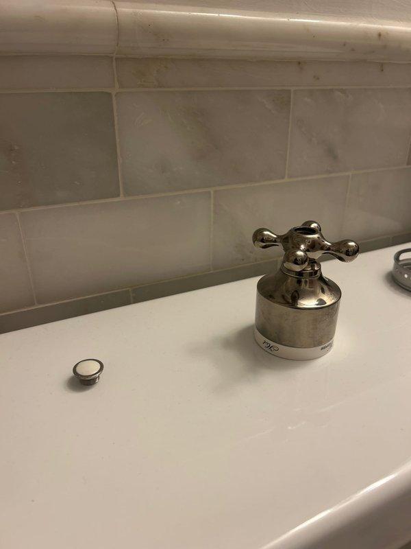 Completed installation of traditional-style chrome bathroom fixtures including a brushed nickel soap dispenser at the vanity sink and a polished chrome shower valve with cross-handle design. Both fixtures were mounted on tiled surfaces featuring subway tile pattern at sink area and decorative stone-look tile at shower location, ensuring proper alignment and secure installation for optimal functionality.