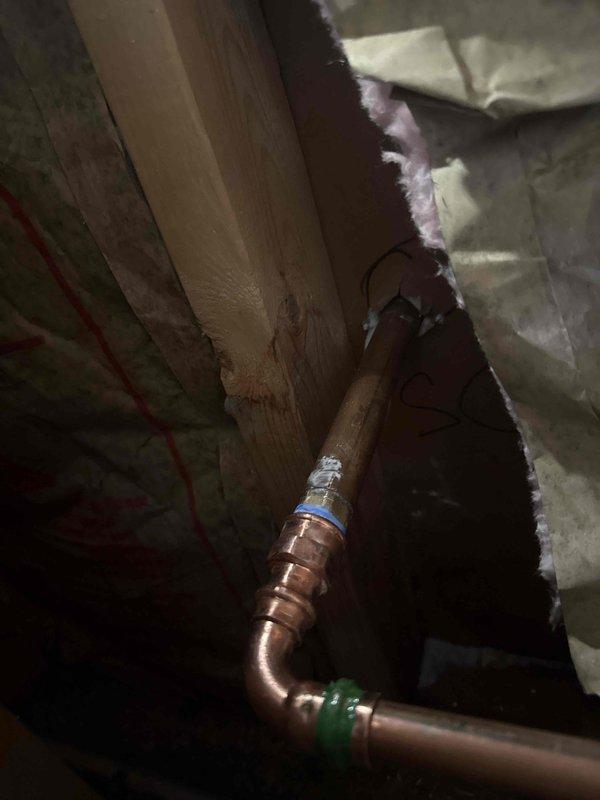 Responded to water leak emergency in residential property. Upon investigation, located source of leak in attic crawl space where copper supply line showed signs of failure at elbow joint connection. Inspected copper piping configuration with brass valve assembly and compression fittings surrounded by fiberglass insulation. Identified compromised joint as cause of water intrusion appearing on interior floor below. Repaired failed connection, tested system under pressure to verify proper seal, and confirmed no additional leaks present in accessible piping throughout the crawl space area.