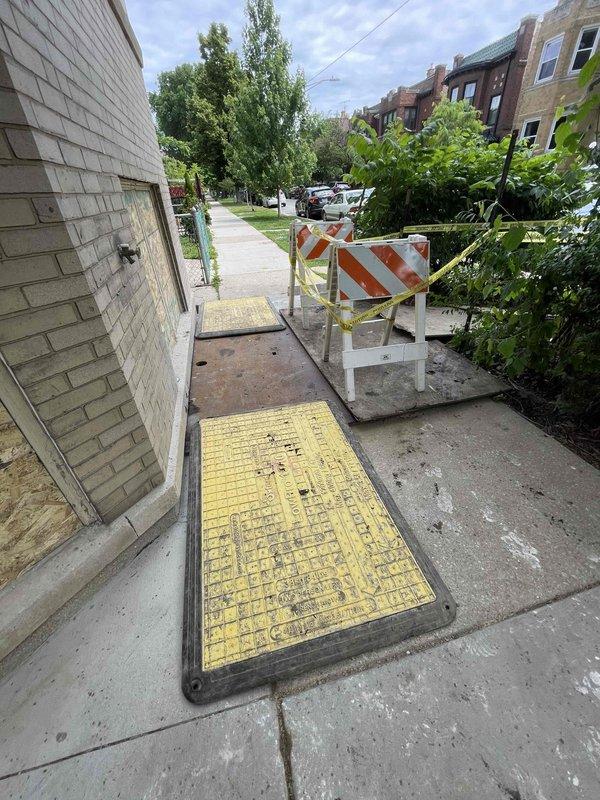 Completed excavation and repair work on residential sidewalk to access underground plumbing utilities. Excavated concrete section approximately 6-8 feet in length to expose subsurface infrastructure, installed proper safety barricades and caution tape around work zone, and provided temporary wooden walkway for pedestrian access. Work area secured with utility access covers and safety measures in place pending final restoration.
