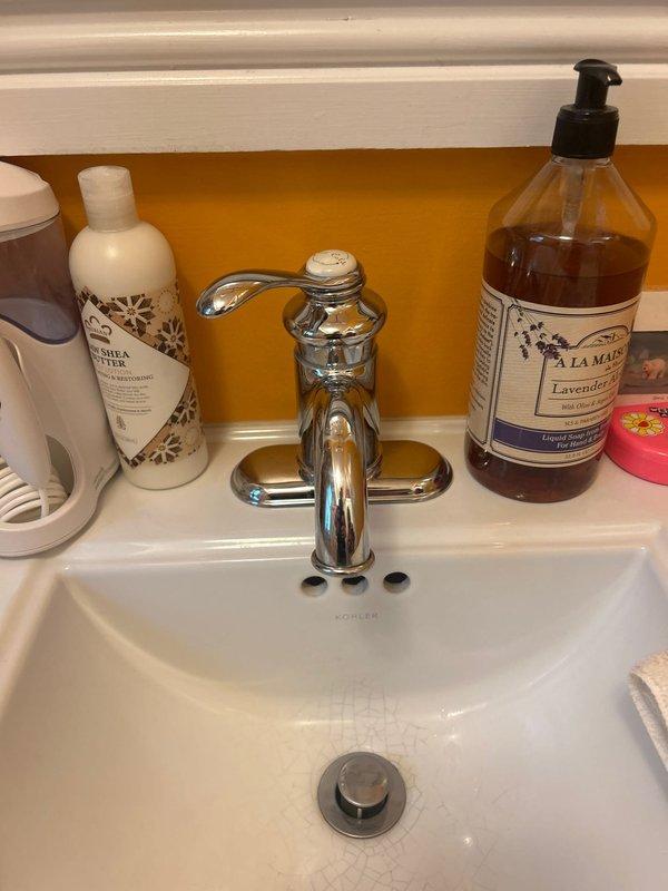Completed installation of chrome single-handle faucet on Kohler bathroom sink with matching decorative cross-handle angle stop valves and braided stainless steel supply lines. All connections tested and verified leak-free with proper water flow and drainage function confirmed.