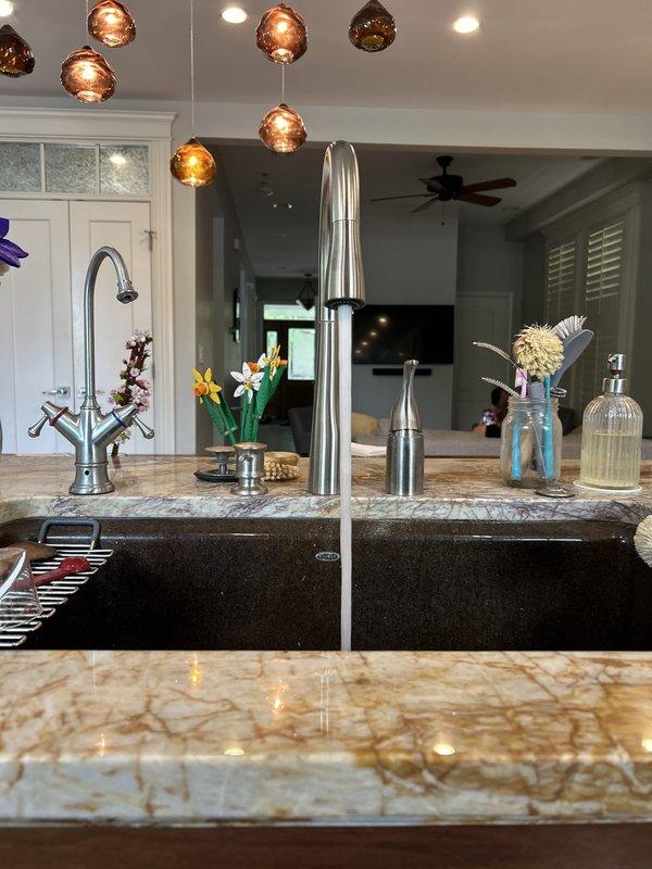 Installed new chrome gooseneck kitchen faucet with dual handles at island sink, connecting supply lines to existing shut-off valves and verifying proper water flow and drainage. All connections tested and confirmed leak-free with no issues detected in the existing under-sink plumbing configuration.