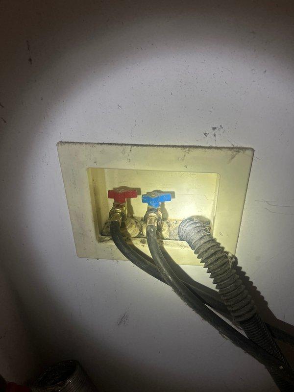 Installed new washing machine supply valves in recessed wall outlet box with hot and cold water connections featuring red and blue handled shutoff valves. Connected flexible braided stainless steel supply hoses to valves to complete the fixture installation. Building water supply was shut down at noon to facilitate safe installation of the plumbing fixtures.