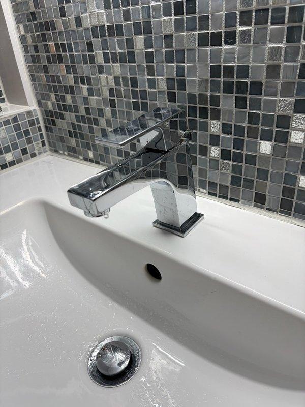 Completed bathroom faucet replacement in residential unit, removing existing 40-year-old fixture and installing new single-handle chrome faucet with contemporary geometric design on white ceramic sink basin. Installation included proper mounting to sink deck, connection to existing supply lines, verification of water flow and drainage function, and confirmation of no leaks at all connection points.