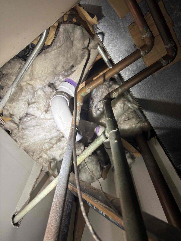 Responded to water leak complaint near water heater in 40-year-old residence where leak had been occurring daily for five days. Upon inspection, accessed ceiling cavity and identified corroded copper piping with significant green patina indicating long-term oxidation and deterioration. Examined plumbing lines running through insulated attic space, noting aging infrastructure with compromised pipe integrity. Documented existing conditions including copper supply lines, PVC drainage pipes, and insulation materials for repair assessment and authorization.