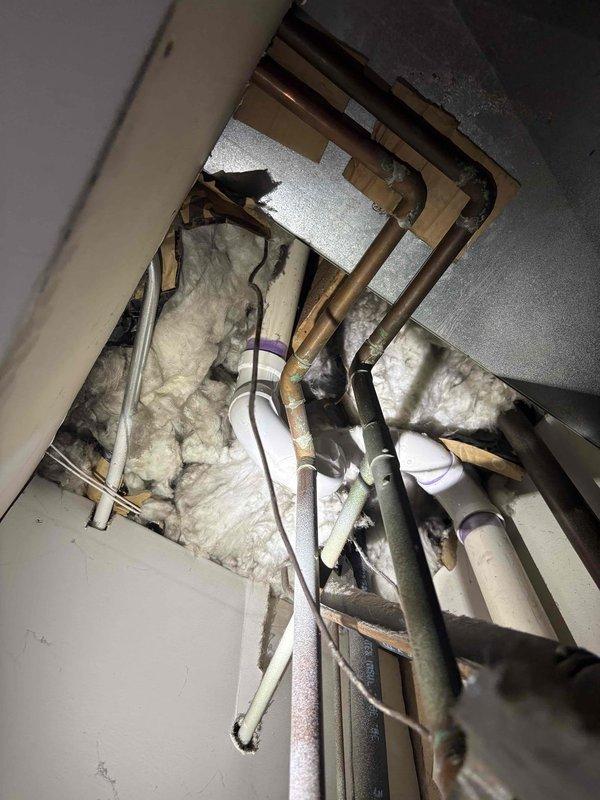 Responded to water leak complaint near water heater in 40-year-old residence where leak had been occurring daily for five days. Upon inspection, accessed ceiling cavity and identified corroded copper piping with significant green patina indicating long-term oxidation and deterioration. Examined plumbing lines running through insulated attic space, noting aging infrastructure with compromised pipe integrity. Documented existing conditions including copper supply lines, PVC drainage pipes, and insulation materials for repair assessment and authorization.
