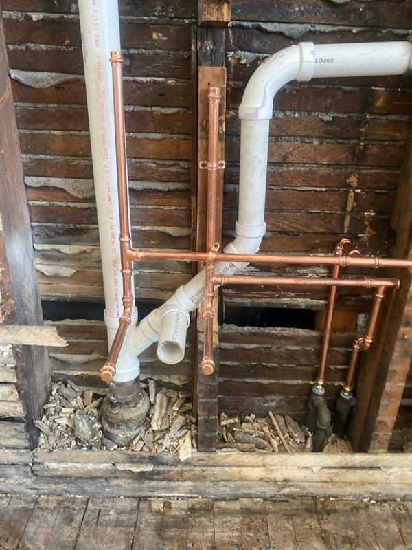 Completed plumbing repair service involving under-sink drainage and supply line components in bathroom setting. Accessed property using provided key code and performed inspection of existing plumbing infrastructure including P-trap assembly, flexible supply lines, and drain connections beneath bathroom sink. Additionally inspected and documented copper and PVC piping configuration in basement/crawl space area showing mixed material plumbing system with multiple connections and joints against exposed brick wall construction.