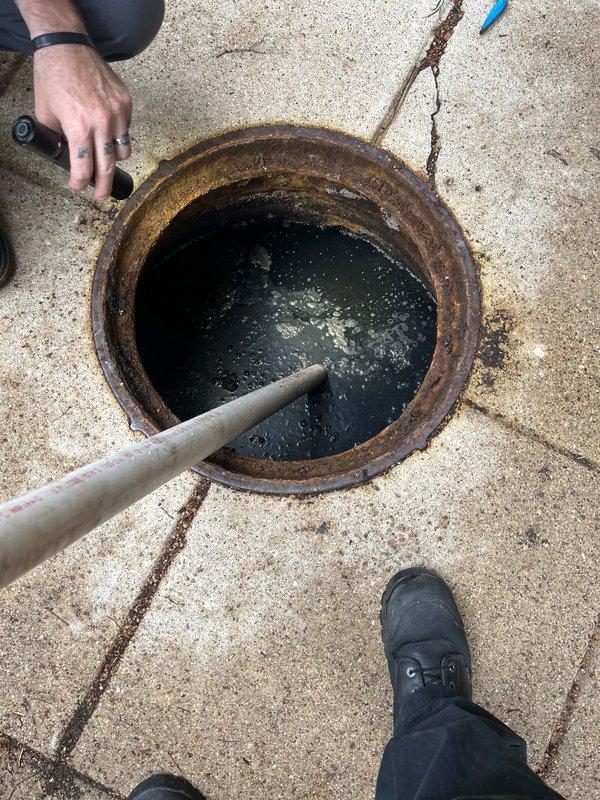 Responded to residential property experiencing multiple sewer backup issues. Accessed main sewer line through exterior cleanout pit, which exhibited severe corrosion and rust on metal rim components indicating long-term moisture exposure. Performed visual inspection of underground sewer infrastructure, documenting heavily deteriorated conditions including stagnant water with debris accumulation, algae growth, and mineral deposits throughout the access point. Recommended implementation of annual sewer maintenance program to prevent future emergency backup situations and address ongoing drainage concerns within the building's sewer system.
