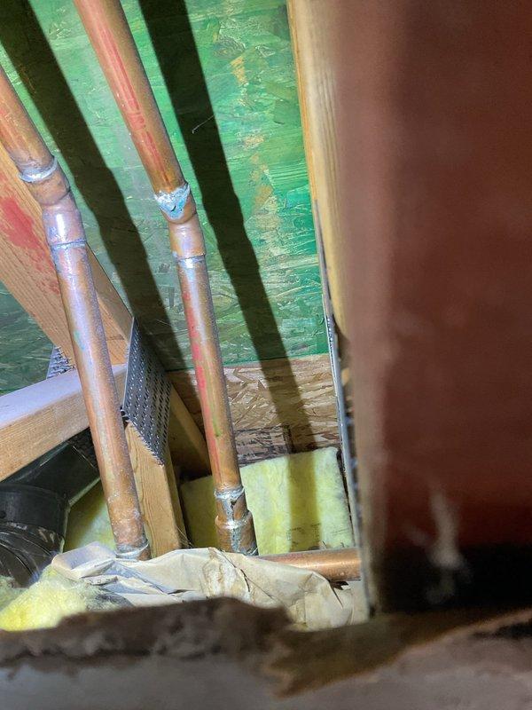Responded to a ceiling leak originating from shower plumbing in a 20-year-old residence. Accessed ceiling cavity below bathroom to locate source of water intrusion. Inspected copper supply lines and connections, identifying compromised pipe fittings as the leak source. Created access opening in ceiling drywall to expose plumbing infrastructure and assess extent of water damage to insulation and framing. Documented existing conditions with photographs showing copper piping, mounting brackets, and saturated fiberglass insulation requiring attention.