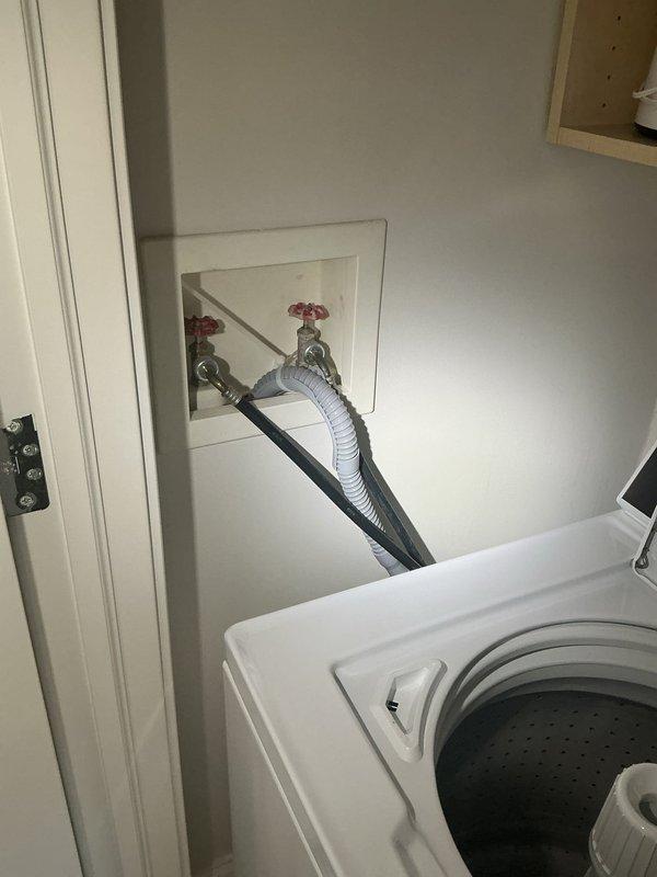 Responded to a callback for laundry appliance plumbing connections. Inspected washing machine water supply lines, shut-off valves with red handles, and flexible hose connections in recessed wall box. Verified proper installation and function of plumbing fixtures serving the top-loading washer unit. All connections were found to be secure and operating correctly.