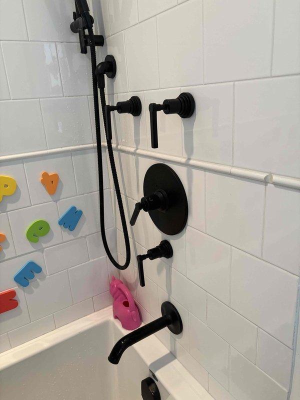 Conducted comprehensive plumbing assessment at 40-year-old residential property requiring fixture replacements and repairs. Evaluated kitchen faucet and cracked sink basin for replacement specifications, inspected bathroom shower thermostatic control valve for heat regulation malfunction, and documented existing plumbing fixtures including matte black shower system with handheld and fixed components. Property access coordinated via phone call due to gated entry, with photographic documentation completed of water heater installation area showing aged mounting hardware with corrosion present, and full bathroom shower/tub assembly featuring subway tile surround and multi-handle temperature control system requiring repair assessment.