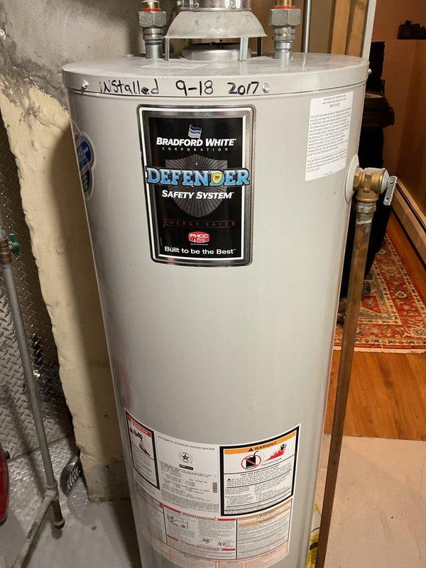 Responded to service call for failed water heater. Upon inspection, found a 9-year-old Bradford White Defender Safety System tank-type water heater installed in the basement utility area that was no longer functioning. The unit, originally installed in September 2017, had reached the end of its serviceable life. Documented the existing installation, including the water heater's condition, surrounding plumbing connections with brass fittings and pressure relief valves, and the utility room configuration with sump pump system and electrical equipment. Provided customer with detailed estimate for water heater replacement, including removal of the existing failed unit and installation of new equipment with proper connections and code-compliant safety devices.