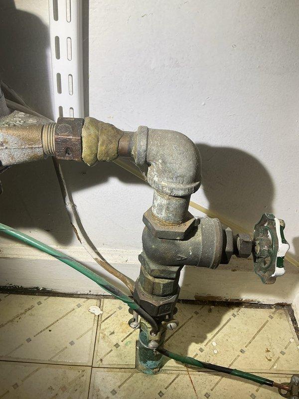 Completed plumbing fixture installation involving aged brass piping system with T-joint configuration and shutoff valve mechanism. Addressed significant corrosion and oxidation on existing pipe connections, replaced deteriorated sections showing greenish-black patina and mineral buildup, and secured new fittings with proper threaded connections and coupling joints to restore functionality.