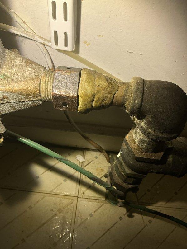 Completed plumbing fixture installation involving aged brass piping system with T-joint configuration and shutoff valve mechanism. Addressed significant corrosion and oxidation on existing pipe connections, replaced deteriorated sections showing greenish-black patina and mineral buildup, and secured new fittings with proper threaded connections and coupling joints to restore functionality.