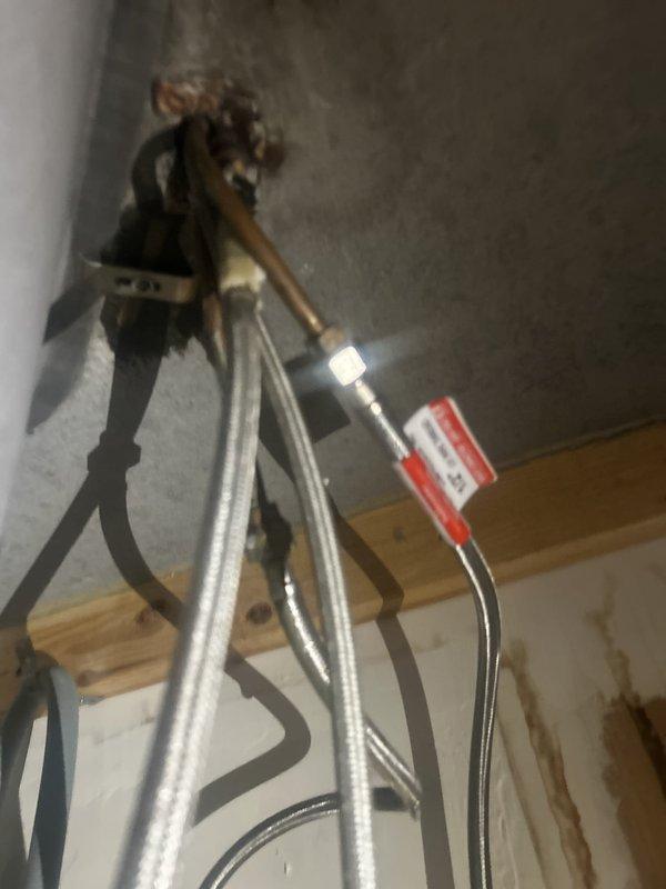 Responded to emergency plumbing service call for kitchen sink leak that required building maintenance to shut off water supply to the unit. Upon arrival, conducted thorough diagnostic inspection of kitchen plumbing system, focusing on the sink drain assembly and faucet supply connections as identified problem areas. Inspected P-trap (J-bend) assembly beneath sink cabinet and examined all visible drain connections for signs of deterioration, loose fittings, or failed seals. Evaluated faucet supply line connections, shut-off valves, and associated plumbing infrastructure in the cabinet space and adjacent areas. Documented existing conditions with photographs showing overhead pipe configuration including copper and metallic supply lines with junction points and valve assemblies, as well as kitchen sink area with modern chrome faucet installation. Identified source of leak and performed necessary repairs to affected components. Tested all repaired connections under pressure to verify prope