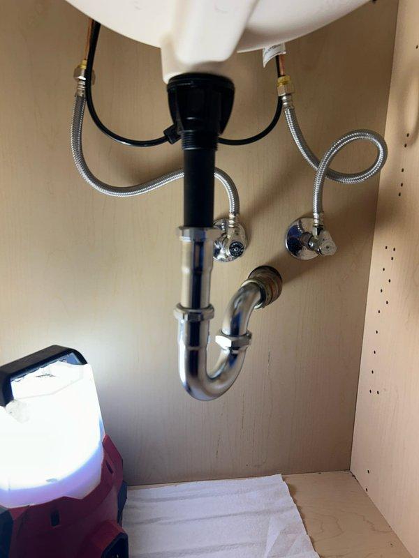 Completed installation of a three-piece widespread bathroom faucet with brushed nickel finish on white porcelain sink. Connected hot and cold water supply lines using braided stainless steel flexible hoses to existing shut-off valves, verified proper water flow and pressure, and tested for leaks at all connection points. Installation includes functional drain assembly with chrome P-trap configuration and garbage disposal unit integration under sink.