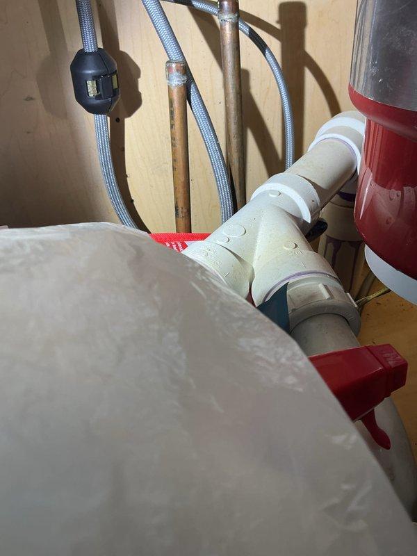 Completed comprehensive plumbing installation involving water heater components, PVC drainage system, and kitchen sink assembly with garbage disposal unit. Installed white PVC pipe network with multiple elbows and T-joints, configured dual-sink drainage system with proper venting, secured all connections with appropriate fittings and metallic hose clamps, and integrated braided stainless steel supply lines with copper piping infrastructure.