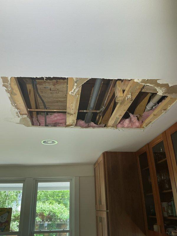 Responded to emergency call for active water leak in kitchen ceiling. Upon arrival, found ceiling already opened with exposed framing and plumbing infrastructure visible. Located failed 1/2" copper water pipe with visible corrosion and green patina in ceiling cavity above kitchen area. Shut off water supply to affected line and removed damaged section of copper piping. Installed new 1/2" copper pipe section using proper fittings and soldered connections to restore water flow. Pressure tested repaired line to verify leak was eliminated and system integrity restored. Confirmed no additional water damage to surrounding pipes or structural components during inspection of exposed ceiling joists and insulation.