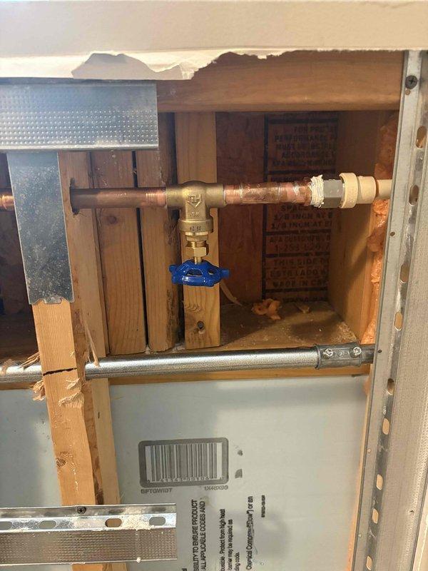 Installed new spigot assembly with copper piping and blue-handled ball valve shut-off within wall cavity. Accessed interior plumbing through existing opening, connected copper pipe to brass fittings, and integrated flexible stainless steel tubing to complete water supply line installation.